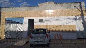 Un coche blanco estacionado frente a un edificio con entrada protegida por una puerta y un cartel que indica un albergue.