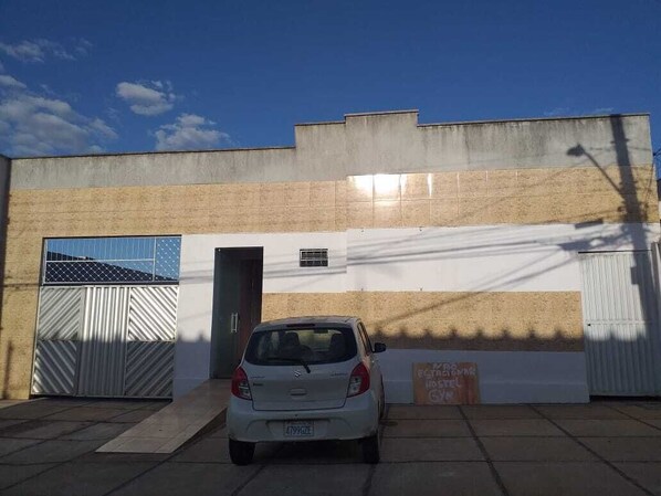 A white car parked in front of a building with a gated entrance and a sign indicating a hostel. - Hostel Goiânia.. (Goiania)