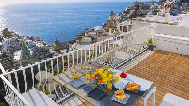 Ein Balkon mit Frühstückstisch, mit Blick auf eine Küstenstadt und das Meer.