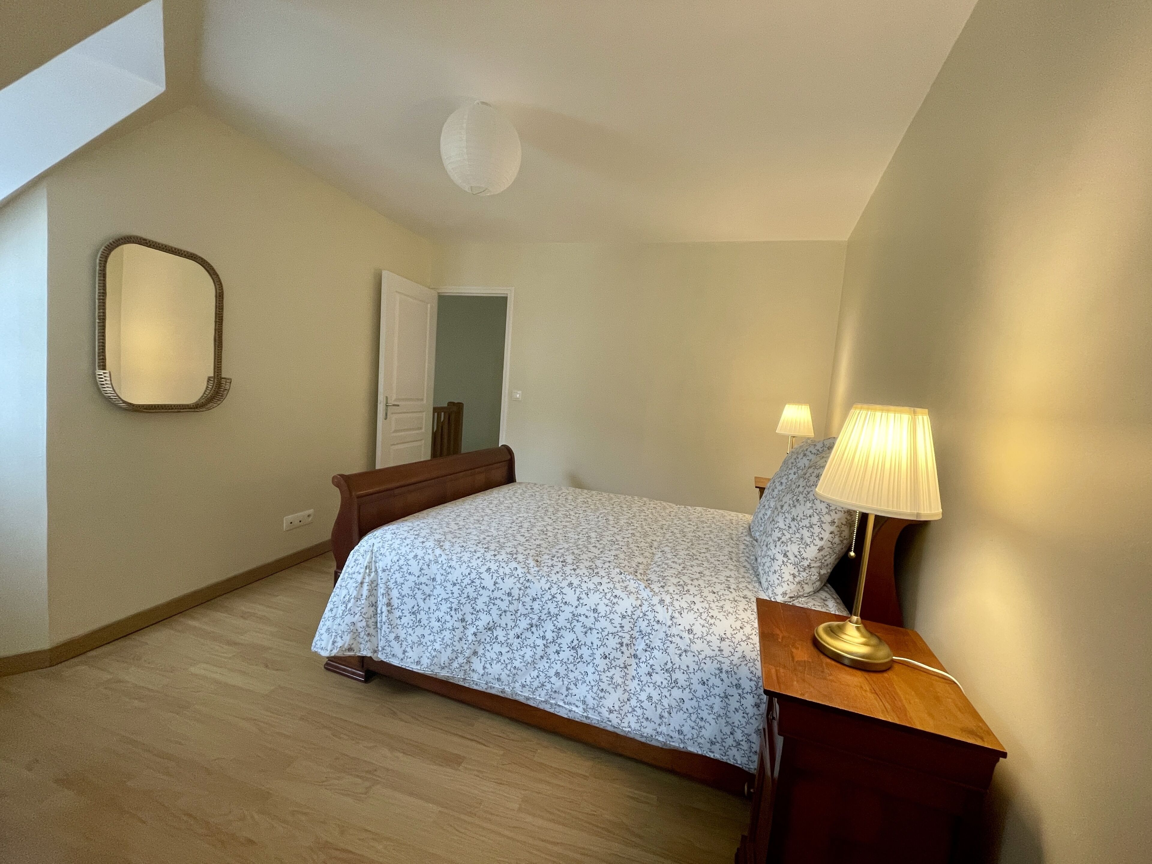A bedroom with a bed, a nightstand, a lamp, a mirror, and a door.