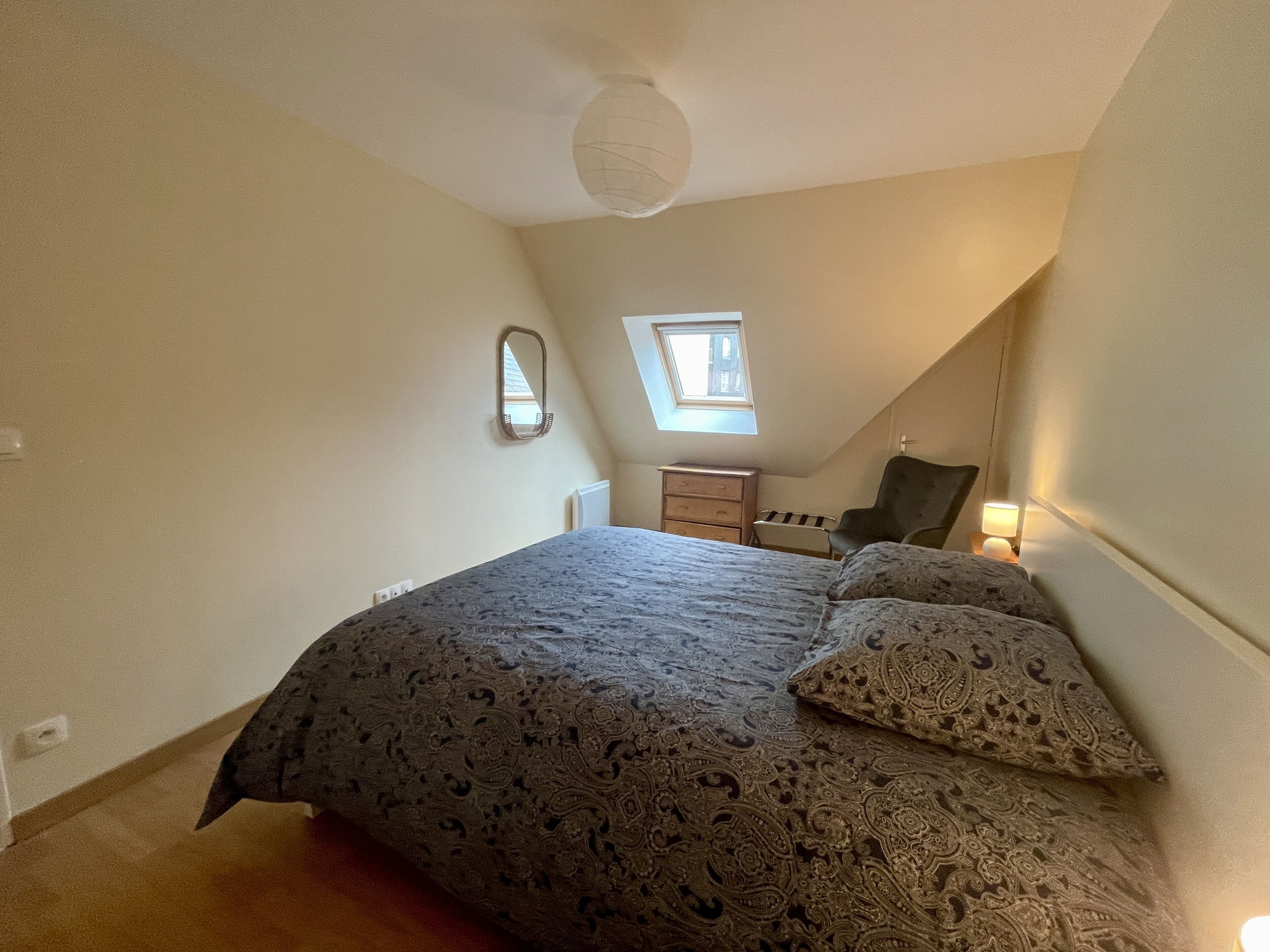 A bedroom with a bed, a dresser, a chair, and a small window.