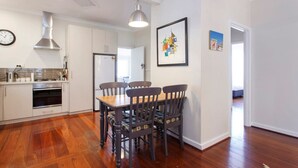 A modern kitchen with white cabinets, a stainless steel range hood, and a dining area with a wooden table and four chairs. - Home Away - 2 Bedroom Cottage (Hilton)