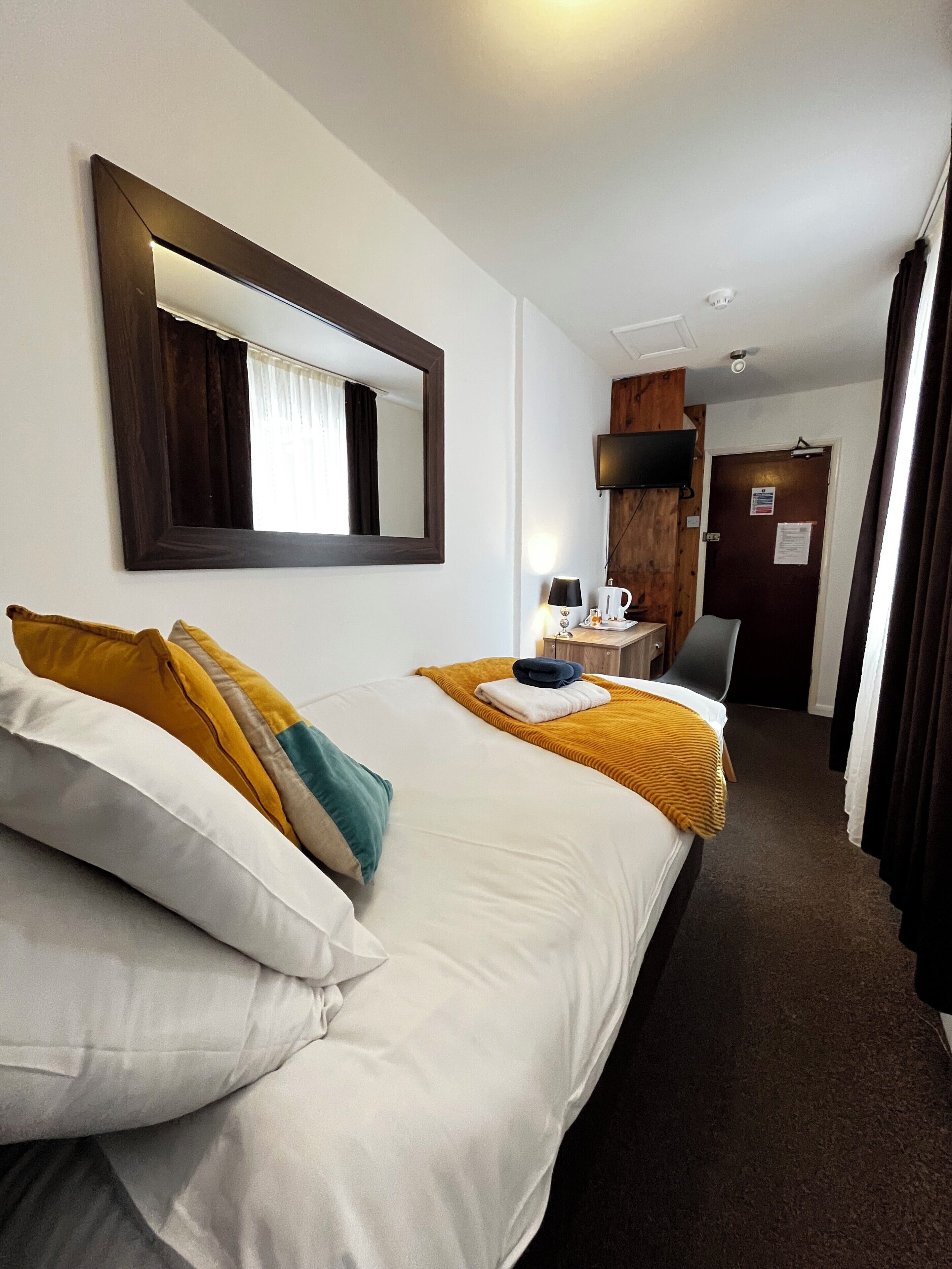 Quarto de hotel com duas camas, um espelho grande, televisão, escrivaninha com abajur e uma porta com placa.