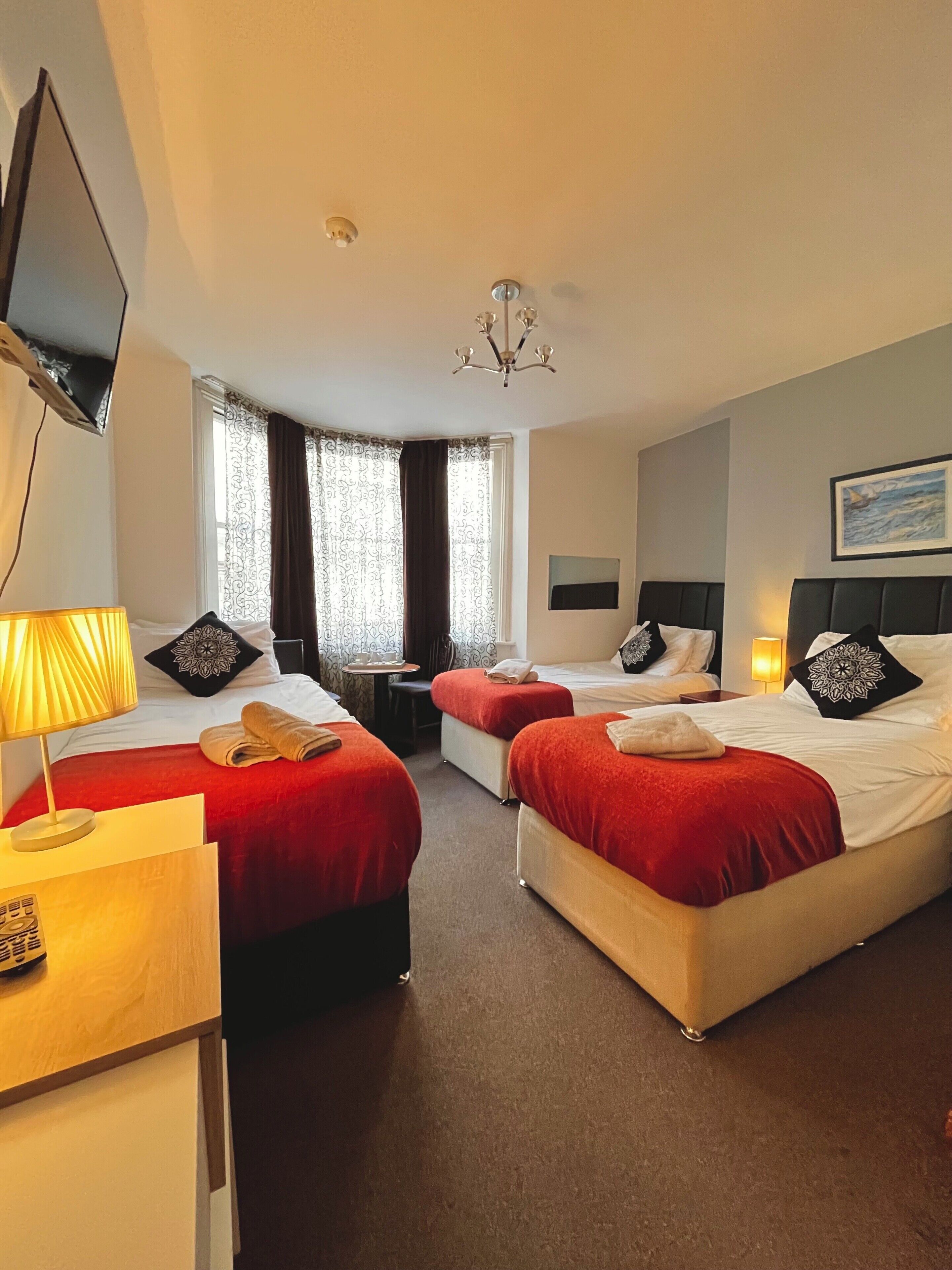 Habitación de hotel con dos camas, televisión, escritorio, silla y ventana con cortinas.