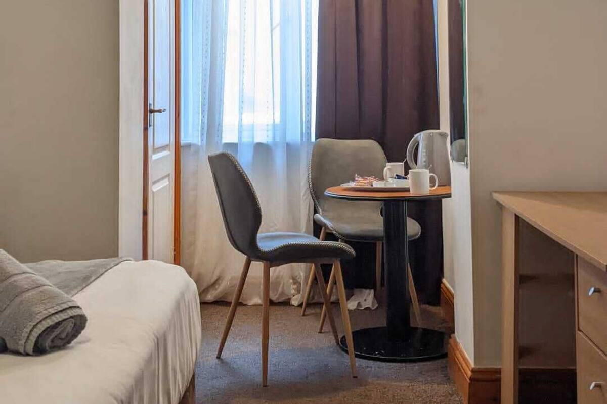 A compact hotel room with a bed, a desk, a chair, and a small table.