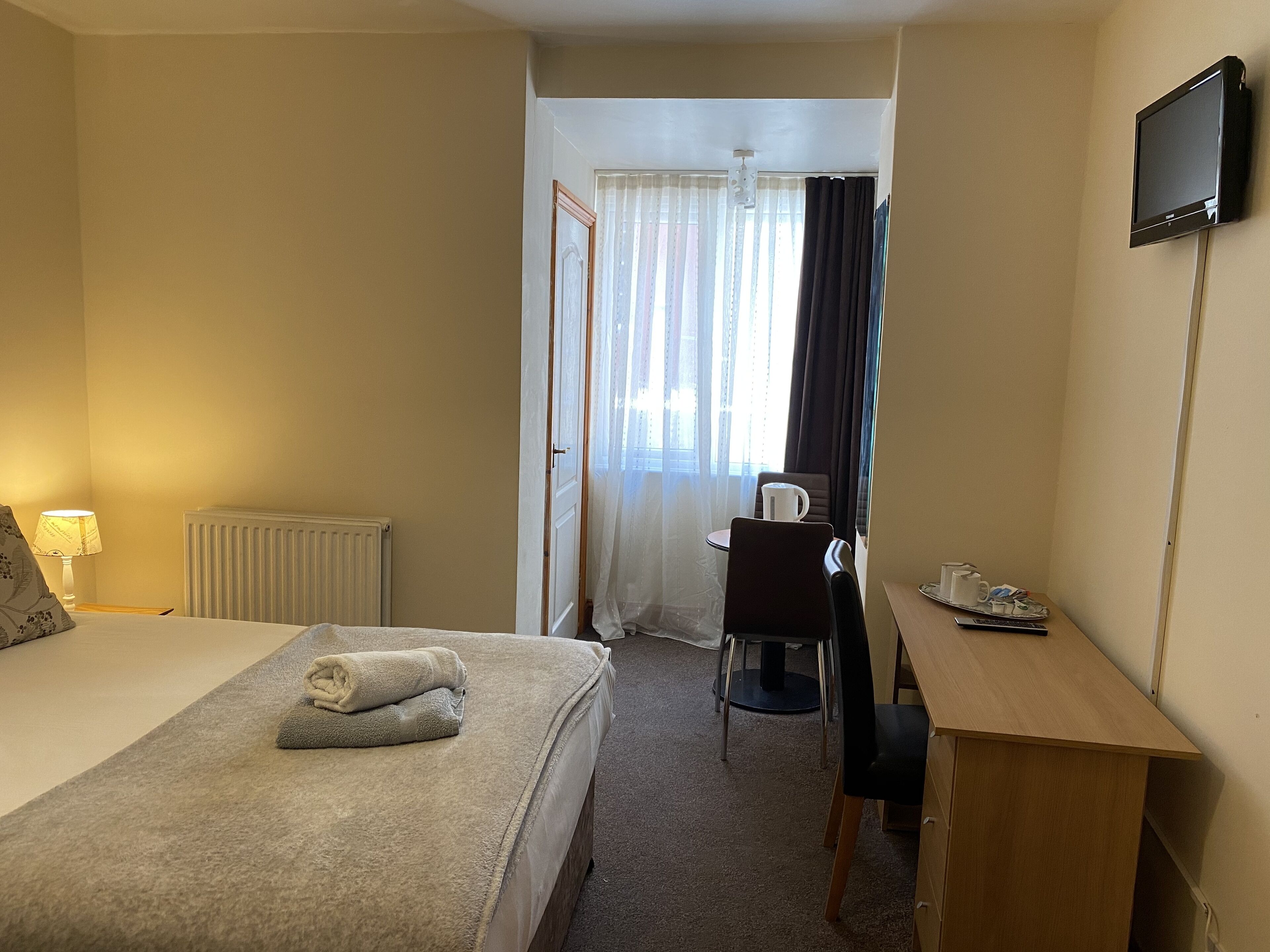 A hotel room with a bed, a desk, a chair, a television, and a window with curtains.