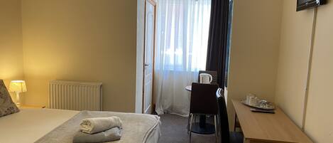 A hotel room with a bed, a desk, a chair, a television, and a window with curtains.