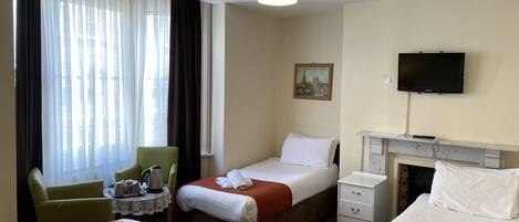 A hotel room with two beds, a television, a fireplace, and a window with curtains.