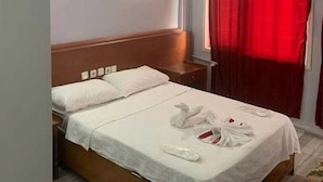 A hotel room with a bed, a nightstand, a wall-mounted air conditioner, and a window with red curtains. - mardin konağı (Mardin)