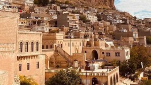 A densely packed hillside town with historic architecture, a prominent rocky hill, and a flag atop a building. - mardin konağı (Mardin)
