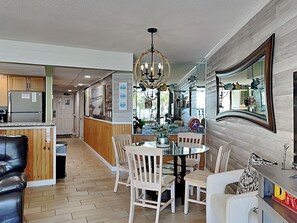 A modern kitchen with wooden cabinets, a stainless steel refrigerator, and a dining area with a glass table and white chairs.