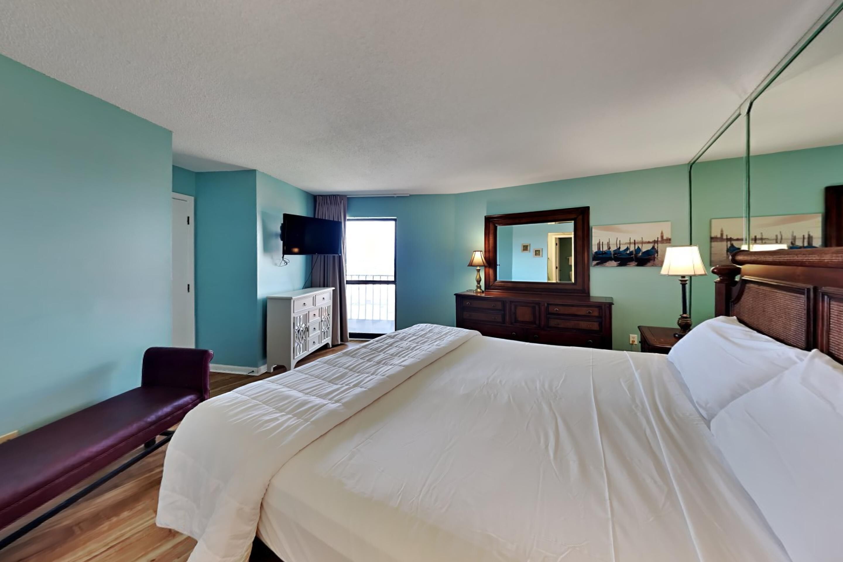 A hotel room with a large bed, a bench, a TV, a dresser, and a window.