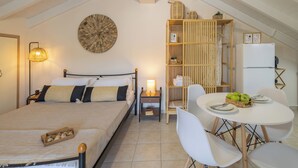 A bedroom with a bed, bedside table, lamp, and a dining area with a table and chairs. - City Suite - The Loft in Kefalonia (argostoli)