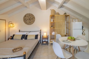 A bedroom with a bed, bedside table, lamp, and a dining area with a table and chairs. - City Suite - The Loft in Kefalonia (argostoli)