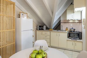 A compact kitchen with a refrigerator, microwave, toaster, and a dining table with a bowl of apples.