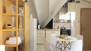 A compact kitchen with a microwave, oven, and a dining area with white chairs and a table. - City Suite - The Loft in Kefalonia (argostoli)