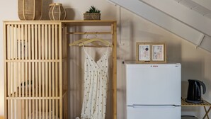 A kitchenette with a white Bosch refrigerator, wooden shelves, a hanging garment rack, and a small plant. - City Suite - The Loft in Kefalonia (argostoli)