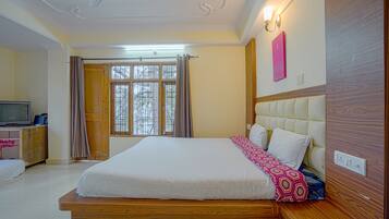 A bedroom with a large bed, wooden headboard, a television on a wooden cabinet, and a window with curtains.