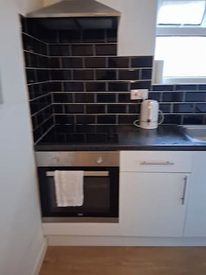 A kitchen with black tiled backsplash, a coffee maker, a stove, and a window.