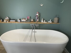 A bathroom with a freestanding bathtub, a shelf with toiletries, and a wall-mounted bird sculpture. - Hitton Séjours Nature (Biran)