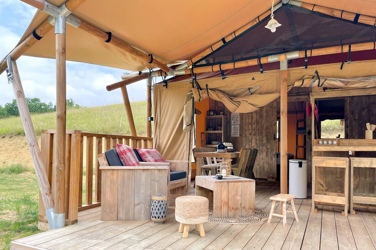 A wooden deck with a sofa, table, and chairs under a large tent.