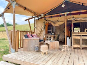 A wooden deck with a sofa, table, and chairs under a large tent. - Hitton Séjours Nature (Biran)