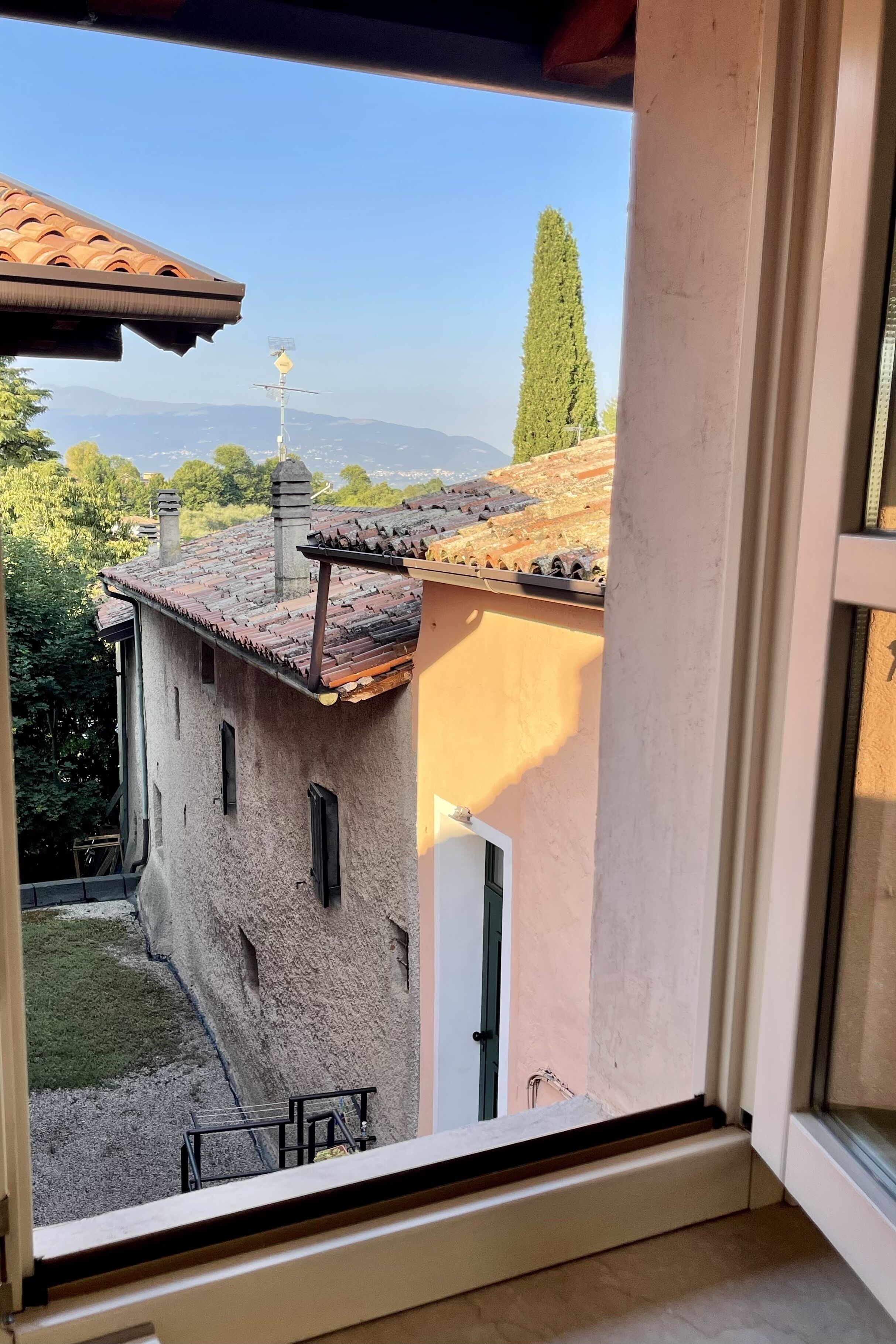 A view from a window of a building with a tiled roof, a small garden, and a distant mountain range.