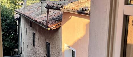 A view from a window of a building with a tiled roof, a small garden, and a distant mountain range.