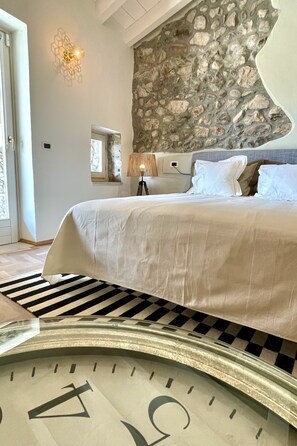 Ein Schlafzimmer mit Steinwand, einem Bett mit weißer Bettwäsche, einer Lampe und einer Uhr auf dem Boden.