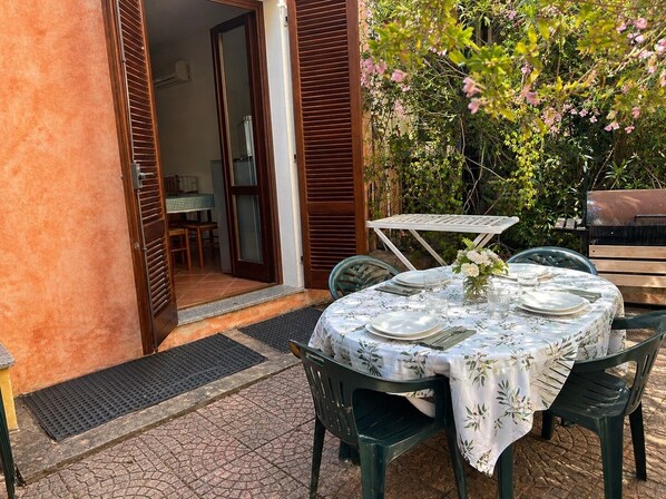 Un espace de restauration en plein air avec une table dressée pour quatre personnes, entouré de verdure et d’une structure en bois.
