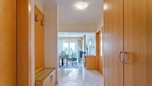 A hallway with wooden doors, a tiled floor, and a view into a dining area with a table and chairs.