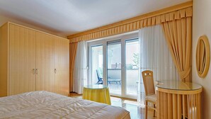 A hotel room with a large bed, a small table, a chair, and a view of the outside through a sliding glass door.