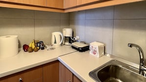 Una cocina con gabinetes de madera, un lavamanos de acero inoxidable, una cafetera y varios alimentos sobre la encimera.