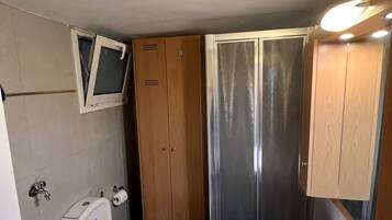 Een kleine badkamer met toilet, wastafel, douche en kast.