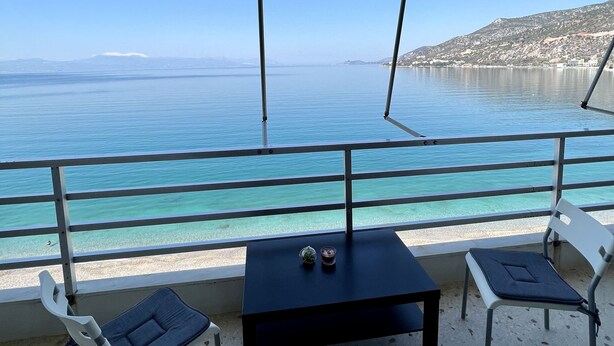 Una terraza con mesa y sillas con vista a un mar azul y un paisaje montañoso.