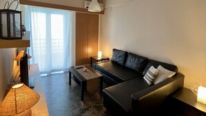 Una sala de estar moderna con un sofá de cuero negro, una mesa de centro y un mueble para televisor. Se aprecia un ventanal con cortinas, una lámpara de techo y un suelo con diseño de piedra.