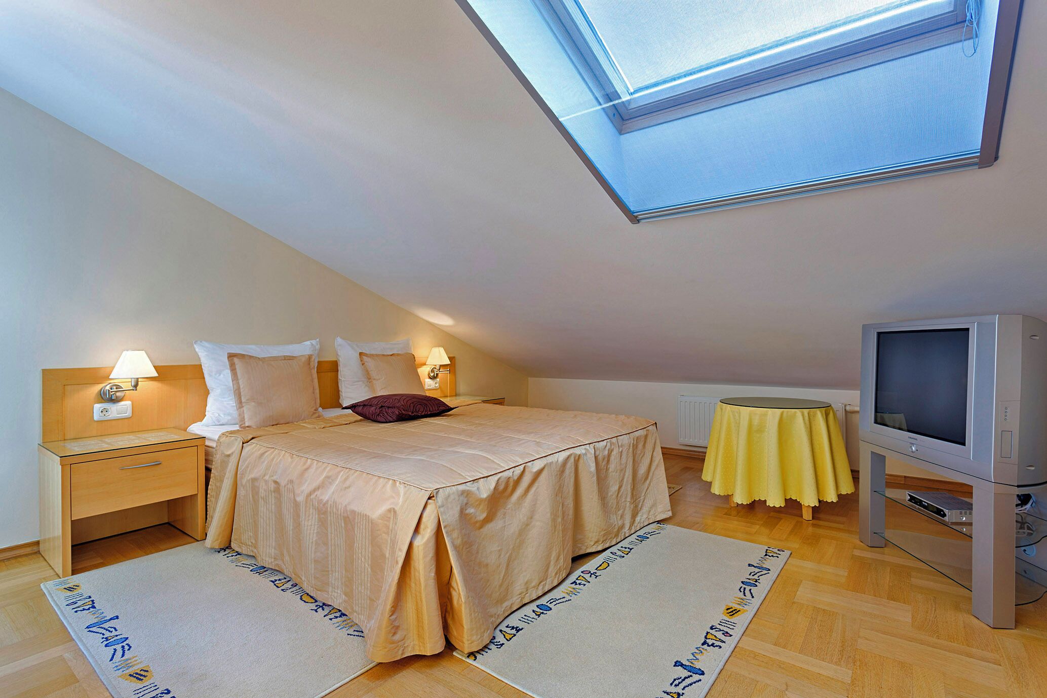 Une chambre à coucher avec un lit, des tables de chevet, une télévision et une lucarne.