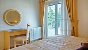 Une chambre à coucher avec un lit, un bureau, une chaise, un miroir rond et une fenêtre avec des rideaux.