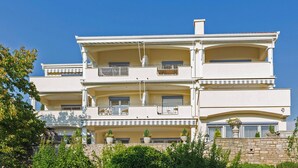 Un immeuble à plusieurs étages doté de balcons, de plantes en pot et d’un mur en pierre.