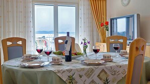 A dining table set with plates, cups, and wine glasses, a bottle of wine, and a bowl of fruit.