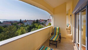 A balcony with a view of houses and greenery, a striped chair, and a glass door leading to an interior space.