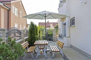 Relax in a shaded outdoor seating area with a table and benches, surrounded by a stone wall and a small tree.