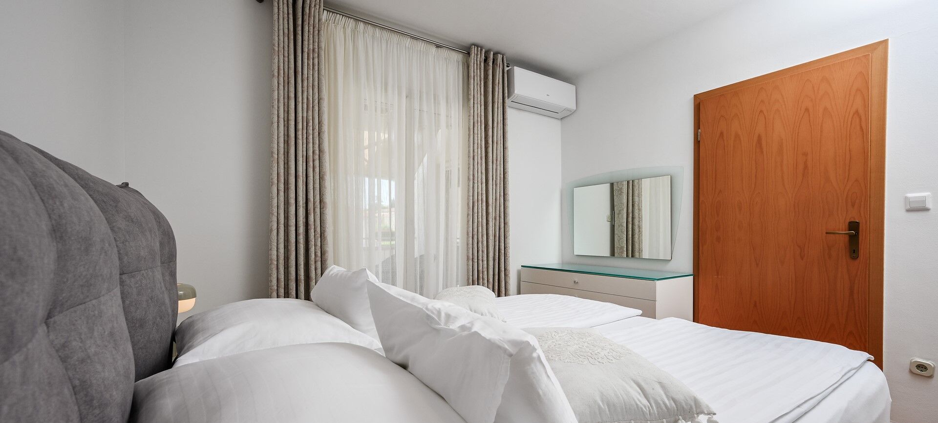 A bedroom with a bed, a bedside table, a mirror, and a wooden door.