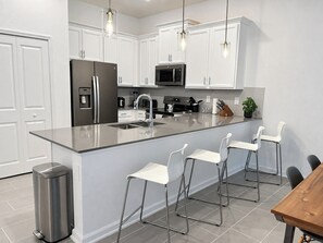 A modern kitchen with white cabinetry, stainless steel appliances, and a central island with bar stools.