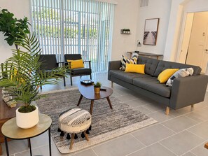 Un salon moderne avec un canapé gris, deux fauteuils, une table basse, un tapis à motifs et une plante en pot.