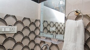 A bathroom with a white sink, a mirror, and a towel hanging on a metal ring. The walls have a patterned wallpaper.