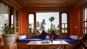 A wooden cabin with a bench by a window overlooking a forest.