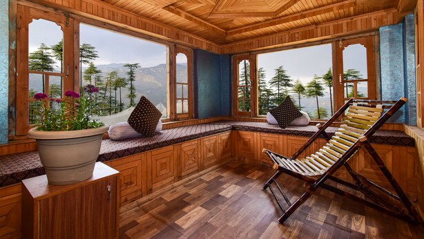 A wooden cabin with large windows, a cushioned bench, and a hanging chair.