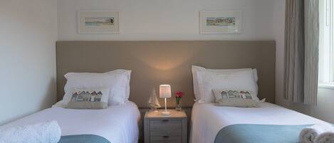 A twin room with two beds, a nightstand with a lamp, and two framed pictures on the wall.