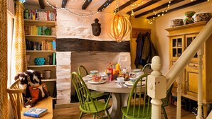 Un rincón comedor acogedor con una mesa redonda, sillas verdes y una estantería llena de libros.